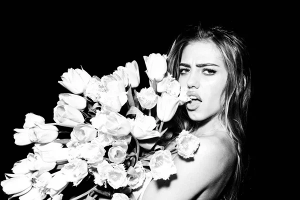 Jonge vrouw met bloemen. mooi meisje holding boeket van tulpen over zwart achtergrond plakken tong met sexy expressie. — Stockfoto
