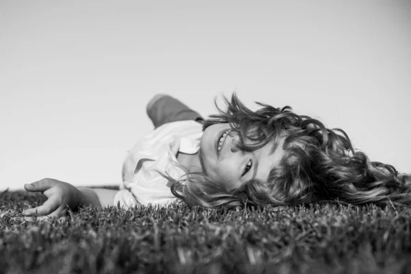 Junge liegt auf dem grünen Gras. Glückliches Kind, das im grünen Frühlingsfeld vor Himmelshintergrund spielt. Freedom Kids und Imagination Konzept. — Stockfoto