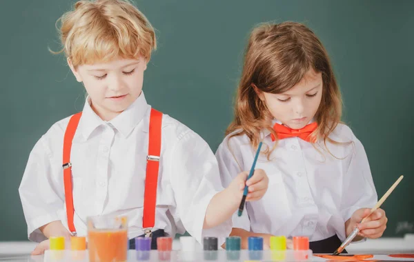 Grappige leerlingen tekenen in de klas op schoolbord achtergrond. School vrienden kinderen jongen en meisje schilderen samen in de klas. — Stockfoto