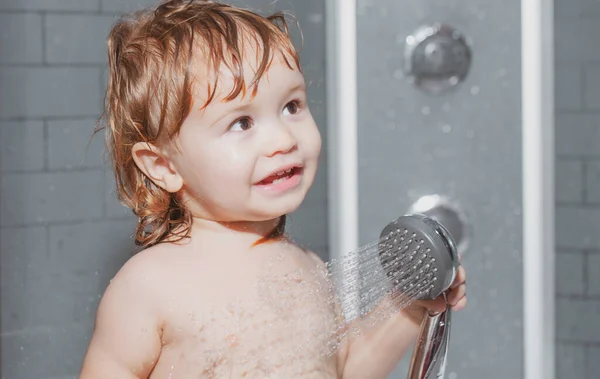 Αστεία χαρούμενα παιδικά λουτρά σε μπανιέρα με νερό και αφρό. Το παιδί κάνει μπάνιο κάτω από ένα ντους. Υγιεινή των παιδιών. — Φωτογραφία Αρχείου