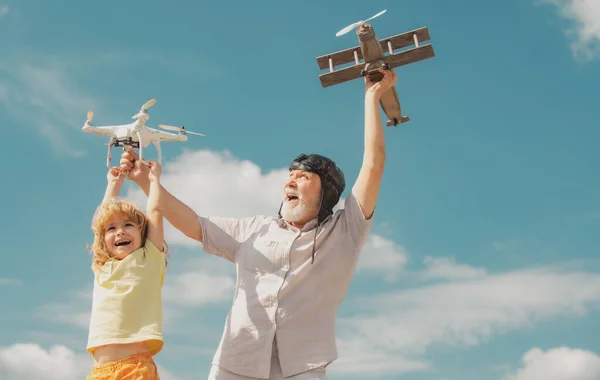 空に対しておもちゃの飛行機とクワッドコプターの無人機で遊んで孫の子供と祖父。飛行機旅行の夢を持つ子供のパイロット航空機。家族関係祖父と子. — ストック写真