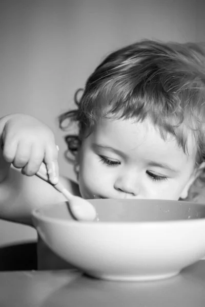 Kind baby eet soep in de keuken met borden en lepel. — Stockfoto
