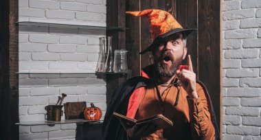 Korku ile Korkunç yüz adam gökyüzü arka planda Kabak baş jack fener tutarak makyaj. Siyah pelerinli kızıl saçlı ve sakallı şeytani bir büyücü büyü kitabı okuyor. Cadılar Bayramı, tatil kutlamaları.