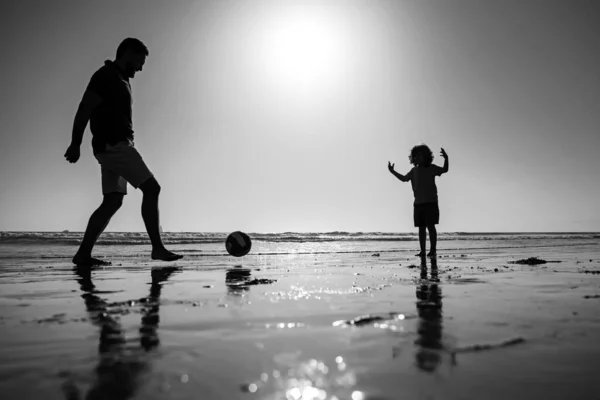 父と息子は夏休みにビーチでサッカーやサッカーをします。父と子供が屋外で遊ぶ、日没のシルエット. — ストック写真