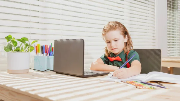 Cute uczennica dziecko odrabia pracę domową z tabletu lub laptopa w domu. Uczeń zapisuje to zadanie w notesie. Kształcenie i uczenie się, edukacja domowa dzieci. — Zdjęcie stockowe