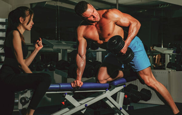 Trainer dumbbell exercises. Boodybuilder couple. Personal friend helping woman working with heavy dumbbells in gym. Sportsman concept. Sport woman.