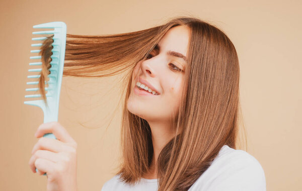 Woman is making hairstyle with comb. Beautiful young woman holding healthy and shiny hair, studio.