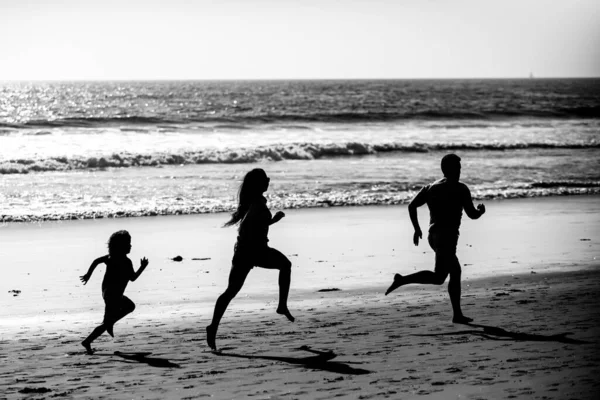 Familia de fitness corriendo en una playa de arena. Deportivo padre de familia, madre e hijo bebé corriendo juntos. Niño con padres regados por el agua a lo largo del mar. Deporte, salud en verano. Estilo de vida saludable. —  Fotos de Stock