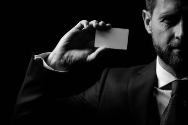 Siyah kostümlü ve kırmızı kravatlı bir işadamı kredi kartı ya da kartvizit gösteriyor. Kapatın. Elinde boş bir kredi kartı modeli var. Kredi kartı, kol tutma şablonu oluşturur.