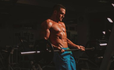 Spor adamı halter kaldırarak biceps yapıyor. Çıplak gövdeli genç kaslı adam spor salonunda çalışıyor. Spor yapan atletik erkek sporcu. Spor konsepti.