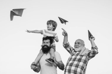 Babalar günün kutlu olsun. Mutlu dedesi baba ve torun mavi gökyüzü ve bulutlar arka plan üzerinde oyuncak kağıt uçak ile. Uçma hayali. İnsan üretimi ve büyüme aşamaları.
