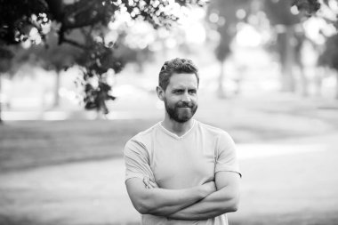 Yaz parkında kollarını kavuşturmuş tişörtlü yakışıklı bir genç..