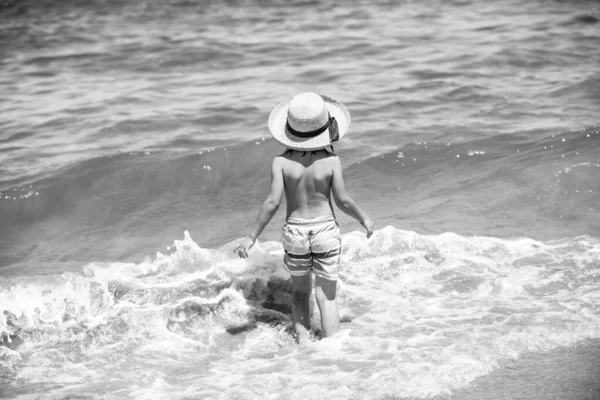 Vue arrière du petit garçon en chapeau de paille à la plage de la mer. — Photo