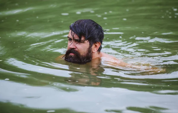 Een man met baard die in de rivier zwemt. Zomervakantie en reizen. — Stockfoto