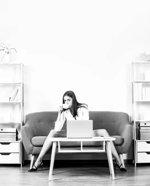 Verführerische Sekretärin mit sexy Beinen, Kaffee trinkend, auf dem Sofa im Büro sitzend. Sexy Geschäftsfrau. Sinnliche Mädchen Mitarbeiter. — Stockfoto