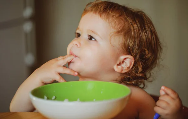 Portrét zábavného malého chlapečka, jak jí z talíře a drží lžíci.. — Stock fotografie