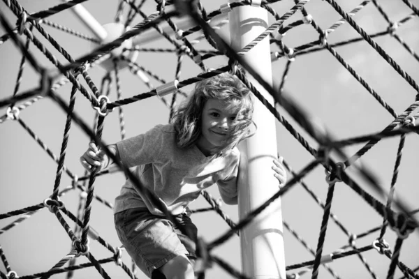 Un ragazzino che si arrampica nel parco giochi della scuola. Faccia divertente per bambini. — Foto Stock