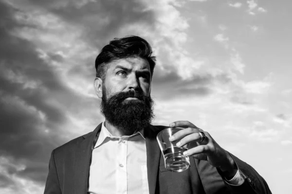 Mann mit Bart hält Glasschnaps, trinkt Cognac. Guy Hipster schmeckt Drink. Whisky schlürfen. Luxus-Nachtleben, reicher bärtiger Mann trinkt teures Getränk. — Stockfoto