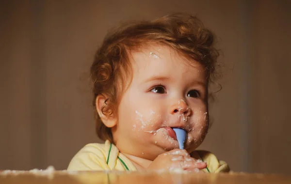 Miúdos a comer com a cara suja. Criança sorridente alegre come-se com uma colher Bebê comendo com rosto sujo. Criança sorrindo comendo comida na cozinha. Criança com fome para que os pais o alimentem. — Fotografia de Stock