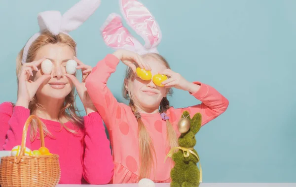 Szczęśliwa rodzina przygotowuje się do Wielkanocy. Matka i córka malują jajka. słodkie małe dziecko dziewczyna noszenie królicze uszy. — Zdjęcie stockowe