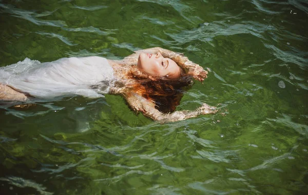 Ung kvinna flyter i hav eller havsvatten, koppla av och ta hand om sig själv. Mode porträtt av graciös söt flicka i sommarklänning under semester på lyx resort. — Stockfoto