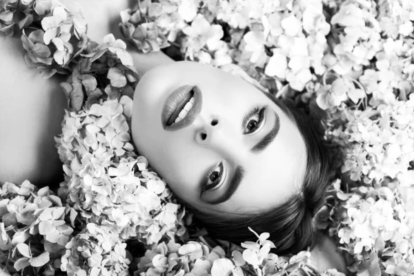 Γυναικεία ομορφιά. Κορίτσι ξαπλωμένο σε λουλούδια. Ενότητα με τη φύση. Μπλόσομ. Προϊόντα μακιγιάζ και περιποίησης δέρματος. — Φωτογραφία Αρχείου