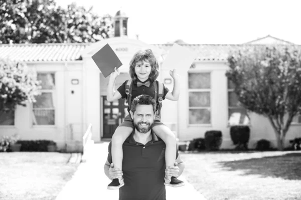 Escuela al aire libre. Padre dando paseo a su hijo a cuestas después de la escuela. El colegial va a la escuela con su padre. Educación para niños. — Foto de Stock