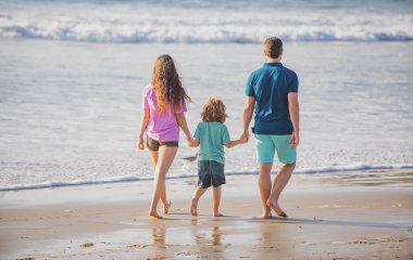 Mutlu aile tatilleri. Neşeli baba, anne, bebek kumsalda yürüyor. Aktif ebeveynler ve insanlar yaz tatillerinde çocuklarla birlikte dışarıda etkinlik yapıyorlar. Aile eğlence aktiviteleri konsepti.