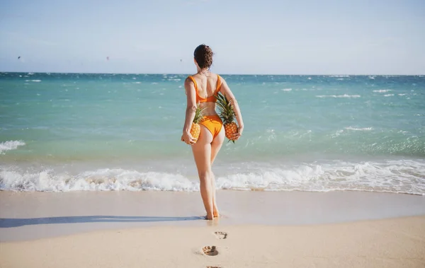 Sexig kvinna med färsk ananas. Rumpor av flicka i bikini med frukt ananas på stranden bakgrund, sommarsemester, hälsosam mat och fitness. — Stockfoto