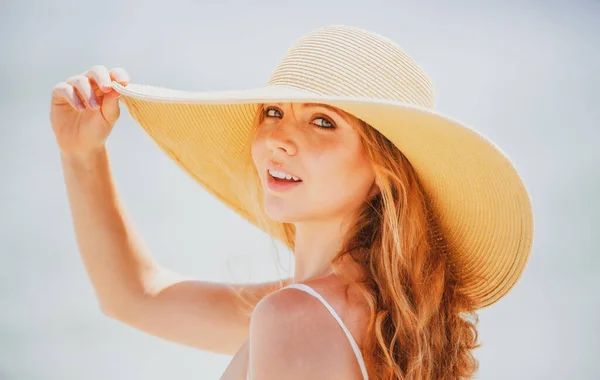 Belle fille avec chapeau de paille profitant du bain de soleil à la plage. Jeune femme bronzée profitant de la brise au bord de la mer. Femme insouciante souriant avec océan de mer en arrière-plan. — Photo