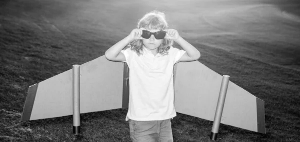 夏の公園でおもちゃの飛行機の翼で遊んでパイロットメガネを持つ子供。革新技術と成功の概念。公園で草の上で楽しんでいる子供のパイロット. — ストック写真