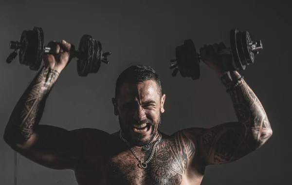 Mladý muskulární Bodybuilder, který provádí cvičení s Dumbrolli nad tmavým pozadím. Intenzivní cvičení. — Stock fotografie