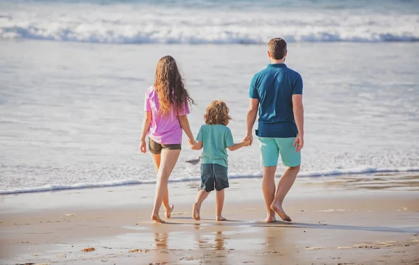 Mutlu aile tatilleri. Neşeli baba, anne, bebek kumsalda yürüyor. Aktif ebeveynler ve insanlar yaz tatillerinde çocuklarla birlikte dışarıda etkinlik yapıyorlar. Aile eğlence aktiviteleri konsepti.