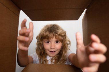 Çocuk karton kutuyu açar ve içinden hediyesini çıkarır. Küçük çocuk paket kutusuna bakıyor ve bir sürpriz aldığına seviniyor. Yüzünde neşe beliren genç bir çocuk. Çocuklar için kutu ve teslimat paketini aç.