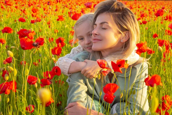 Mutter und Tochter umarmen sich auf dem Frühlingsblütenfeld. Mutter mit Kind in einem Feld mit roten Mohnblumen genießt die Natur. Mutter und kleine Tochter im Mohnfeld. Frau und Kind lachen und umarmen sich. — Stockfoto
