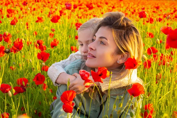 Mãe com a filha abraçada no prado das papoilas. Bela mãe e filha em um campo de papoula ao ar livre. Mãe e filha em flores de papoulas de primavera. — Fotografia de Stock