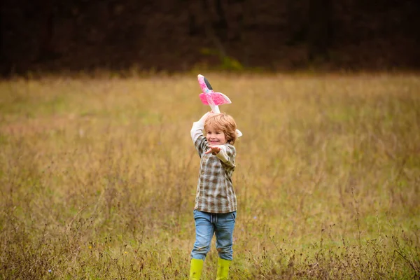 El chico se divierte con el avión de juguete en el campo. Retrato de los niños contra el fondo del cielo de verano en el campo. Concepto de viaje y libertad. — Foto de Stock