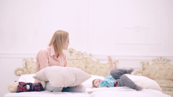 Мама и сын играют с подушкой в спальне. Счастливая мать и маленький сын играют дома в постели. Доброе утро.. — стоковое видео