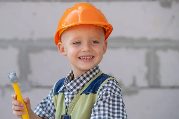 Een jongen met een harde hoed met een hamer. Gelukkig lachend klein kind dat helpt met speelgoedgereedschap op de bouwplaats. Kinderen met bouwgereedschap. Bouwvakker. — Stockfoto