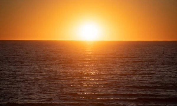Zonsondergang met grote gele zon onder het zeeoppervlak. Rustige oceaan met zonsondergang hemel en zon door de wolken heen. Rustige oceaan en lucht achtergrond. — Stockfoto