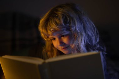 Kitap okuyan şirin bir çocuk. Açık kitabı olan bir çocuk. Ev okulu dersi. Evde kitap okumaya odaklanmış küçük bir çocuk. Yatmadan önce masal masalı.