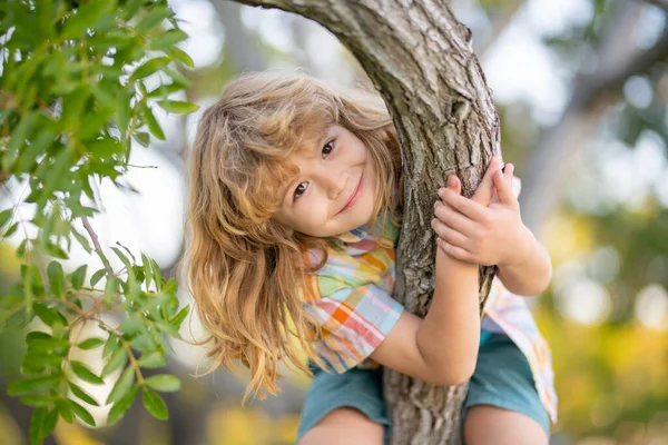 Glückliches Kind, das im Garten spielt und auf den Baum klettert. Junge klettert im Sommerpark auf Baum. — Stockfoto