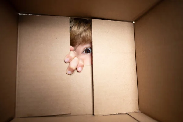 Ενθουσιασμένο παιδί που ψάχνει στο κουτί, στέλνοντας χαρτονένιο κουτί. Κλείσε τα μάτια και κοίτα.. — Φωτογραφία Αρχείου