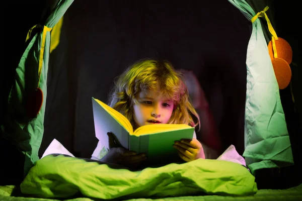 Niño en tienda de campaña para niños leyendo libros. Los niños se enfrentan con luz nocturna. Concepto de educación y lectura. El desarrollo infantil de la fantasía. —  Fotos de Stock