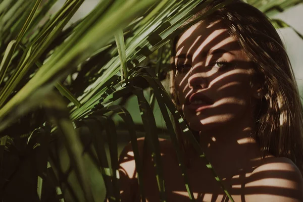 Крупним планом портрет красивої жінки з тінями пальмового листа на її обличчі. Красива молода жінка з оголеним макіяжем виглядає прихованим пальмовим листям . — стокове фото