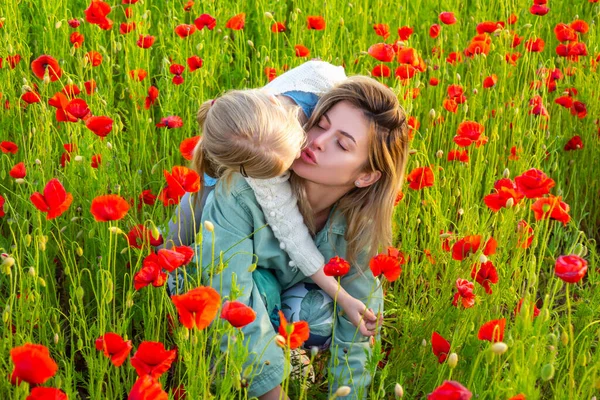 Mutter mit Tochter im Freien im Mohnfeld. Mutter umarmt liebes Kind auf Mohnblumen Hintergrund. Familie auf dem Feld der Frühjahrsblütenwiese. Frau und Kind lachen und umarmen sich. Federentwurf. — Stockfoto