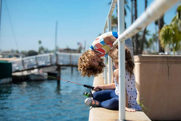 Een jongen die bezig is met vishobby 's, houdt een hengel vast. Zomer kinderen levensstijl. Kinderen vissen in het weekend. Twee jonge schattige kinderen vissen op een meer in een zonnige zomerdag. — Stockfoto