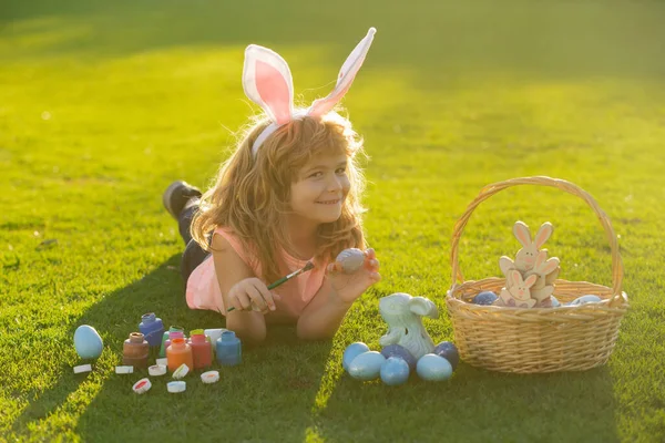 Dziecko z wielkanocnymi jajkami i króliczymi uszami leżące na trawie. Zabawny chłopiec, króliczki wielkanocne. — Zdjęcie stockowe