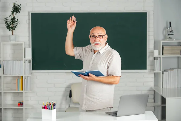 Profesora sénior con libros y pizarra. Viejo profesor sonriente en la universidad. Profesor jubilado varón de edad. —  Fotos de Stock