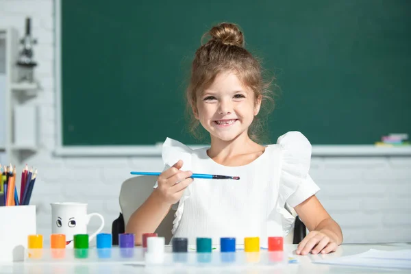 A kislány az iskolában festékkel rajzol. A gyerekek művészi kreativitás. Vicces gyerekek érzelmei. — Stock Fotó